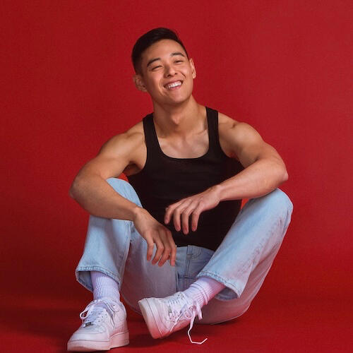 musician Fedge smiling and sitting on a dark red backdrop